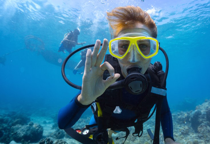 Scuba diver in a yellow mask showing the OK sign